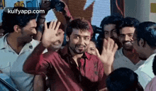 a man in a red shirt is standing in a crowd of people waving his hand .