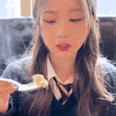 a girl in a school uniform is eating a piece of food with a spoon