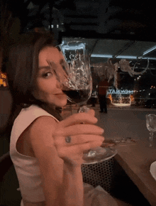 a woman holds a glass of red wine in front of a sign that says " taakom "