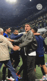 a man in a leather jacket stands in the middle of a soccer field