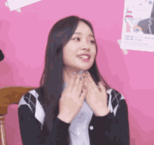 a girl with long black hair is sitting in front of a pink wall with a poster on it