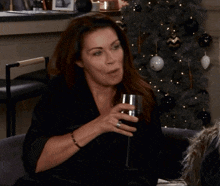two women are sitting in front of a christmas tree one of them is holding a glass of wine