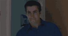 a man in a blue shirt is standing in a doorway looking at the camera .