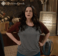 a woman is standing with her hands on her hips in front of a sign that says schitts creek on it