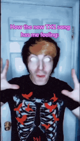 a man wearing a skeleton shirt is standing in front of a door and says how the new tx2 song has me feeling