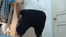 a man in a white tank top and black shorts is squatting in a room