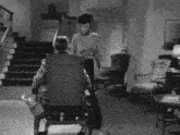 a black and white photo of a man in a wheelchair talking to a woman
