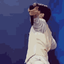 a man in a white vest is singing into a microphone while covering his face with his hand .