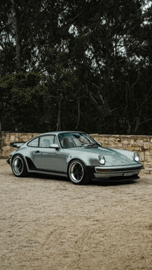 a silver porsche is parked on a dirt road in front of trees