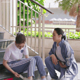 two girls are sitting on the stairs and one has a sticker on her pants that says ' kingofcoffee ' on it