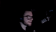 a man wearing glasses and headphones is screaming into a microphone in the dark .