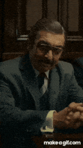 a man in a suit and tie is sitting at a table with his hands in the air .
