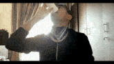 a man wearing sunglasses and a gold chain drinks from a white cup