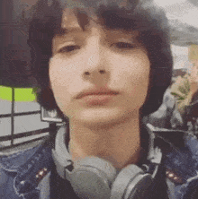 a young man wearing headphones and a denim jacket is taking a selfie .