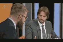 a man in a suit and tie is talking to another man in a suit and tie on a television show .