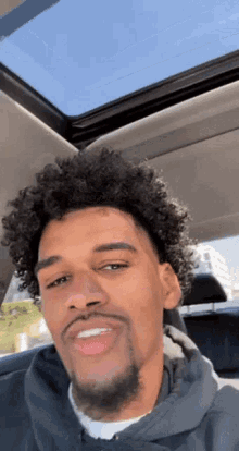 a man with curly hair and a beard is sitting in the back seat of a car with a sunroof .