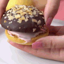 a close up of a person holding a donut with chocolate and nuts on top