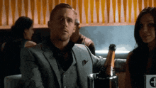 a man in a suit is sitting at a table with a bottle of champagne in a bucket .