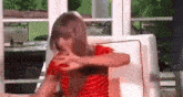 a girl in a red striped shirt is sitting on a couch with her hands on her face .