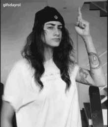 a black and white photo of a woman wearing a beanie and a t-shirt with a butterfly tattoo on her arm