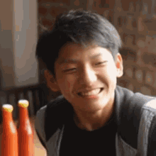 a young man is smiling at the camera while sitting at a table with bottles of sauce .