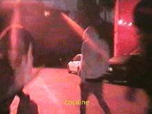 a group of people are walking down a street and the word cocaine is on the bottom right