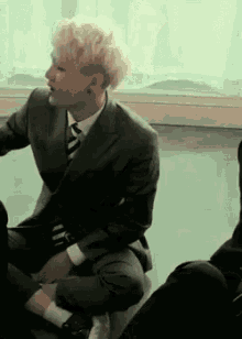a man in a suit and tie is sitting on the floor next to another man .