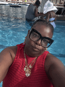 a woman wearing glasses and a red top is taking a selfie in a swimming pool
