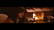 a woman drinks from a glass in front of a fireplace