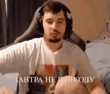 a man wearing headphones and a shirt that says ' завтра не в школу ' on it is sitting in a chair