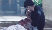 a man is kissing another man laying on the ground with blood on his face .