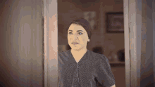 a woman in a polka dot shirt is standing in front of a door and making a funny face .