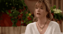 a woman wearing a white sweater and a necklace is sitting in front of a plant .