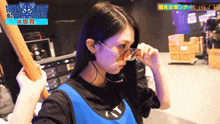 a girl wearing sunglasses and a blue vest is holding a bat