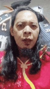 a man with long black hair and a beard is wearing a red shirt