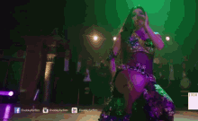 a woman in a purple dress is dancing in front of purple lights