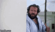 a man with a beard is standing next to a wall .