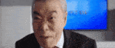 an older man in a suit and tie is looking at the camera in front of a blue screen .