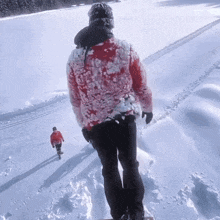 a man in a red jacket and black pants is walking through the snow
