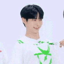 a man in a white shirt with a green star on it is smiling and looking at another man .