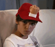 a young boy wearing a red hat is sitting on a couch giving the middle finger