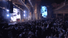 a crowd of people watching a concert with a large screen showing a woman 's face