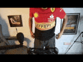 a man wearing a ferrari shirt is standing in front of a chair