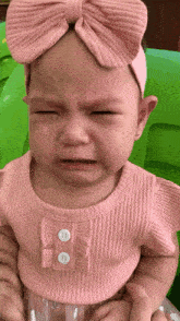 a baby girl wearing a pink headband and a pink shirt is crying