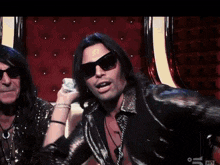 a man wearing sunglasses stands next to another man in a black jacket