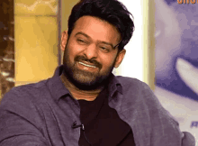 a man with a beard is smiling and wearing a purple shirt and black shirt .