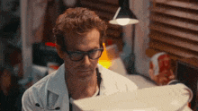 a man wearing glasses and a lab coat looks at a computer screen