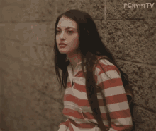 a woman in a red and white striped shirt is leaning against a brick wall .