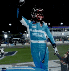 a race car driver wearing a blue safelite uniform stands on the hood of his car