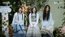 three girls are sitting in front of a tree and a sign that says be lift on it